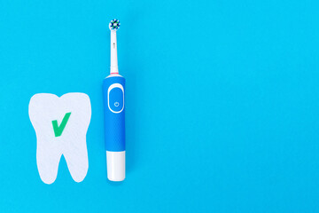 Concept of modern dental care products. Electric toothbrush and a tooth cut out of felt with a green ok icon. Blue background. Flat lay. Copy space