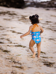 Cute little girl walking on sandy beach. Warm sunny day. Happy childhood. Summer vacation. Holiday at the sea. Baby girl wearing blue swimsuit. View from back. Bali, Indonesia