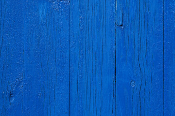 Fototapeta na wymiar Wooden planks painted with deep blue paint. The close-up conveys the texture of the cracked paint well over the texture of the wood. The photo is perfect as a photo background