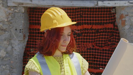 Giovane ragazza ingegnere con caschetto giallo guarda il progetto di fronte al cantiere 