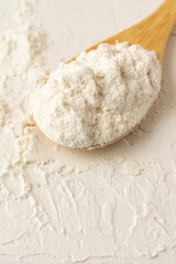 Top view of wooden spoon with flour on white wooden table, vertical, with copy space