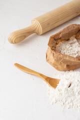 Top view of a pile of flour with wooden spoon, bag with flour and rolling pin, with selective focus, white background, vertical, with copy space