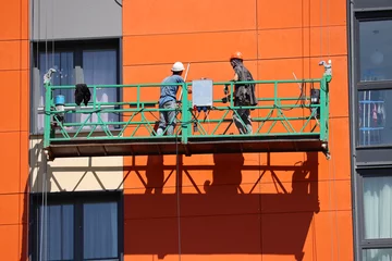 Foto auf Acrylglas Worker standing on lifting platform near the wall of high-rise house. Construction works, residential building facade cladding and insulation © Oleg