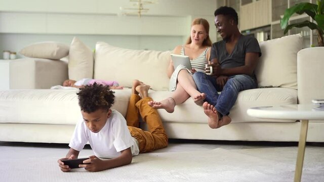 Happy african family spend free time with gadgets in white home interior Spbd