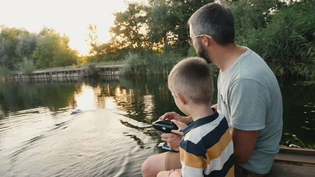 Father and little son play with RC toy speedboat on the lake