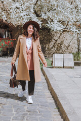 Fototapeta premium smiling pretty woman in jacket and hat walking by spring city street