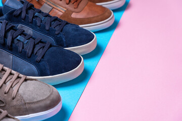 New male's multi-colored sneakers stacked in a row. Shoe tips close-up. Pink and blue background....