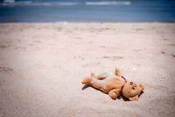 Alone Toy Teddy bear doll sleep on sand beach with blue sea. lonely, sad, broken heart or international missing children's day concept.
