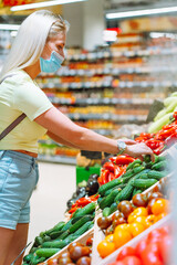Young blonde woman wearing protective mask pick fresh vegetable on stall at market. Woman buying food