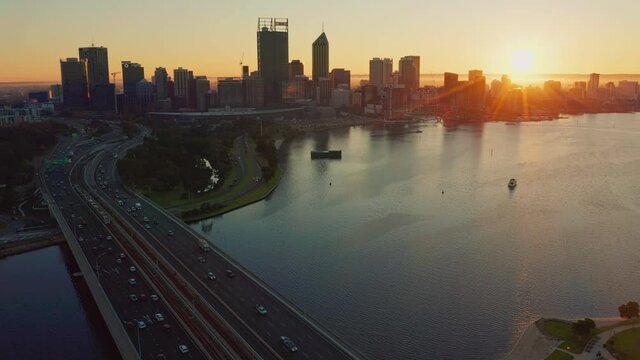 The sun rising on the horizon behind an aerial view of the Perth City skyline and Swan River in Western Australia.