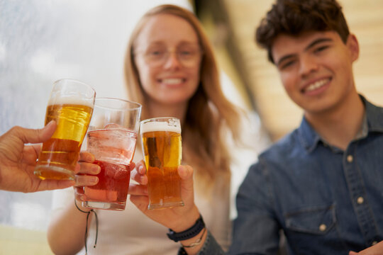 Toast from a group of cheerful multiracial friends sitting on a terrace celebrating with cervesas, having fun during the summer holidays. Celebrations concept