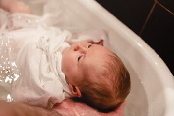 Baby girl, infant bathing. Father hands holding newborn securely. First-time parents, baby-care...