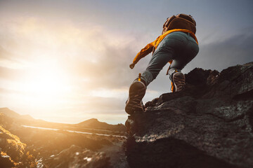 Successful hiker hiking a mountain pointing to the sunset. Wild man with backpack climbing a rock over the storm. Success, wanderlust and sport concept.	
