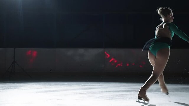 The girl skater performs a jump with the rotation of a triple toe loop in a counter light on an ice cat. Slow-motion jump in figure skating