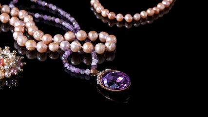 Sparkling purple old amethyst pendant, amethyst beads, and iridescent pearl necklaces on a black background. Luxurious isolated natural jewelry. 