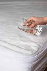 Woman's hand with a glass of water above the mattress in a waterproof case