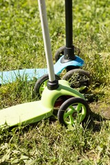 two children's scooters stand on the green grass in the park. children's sports, sports, sports equipment, sports equipment, health, children, urban transport concept