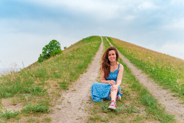 Beautiful young woman in a dress resting on a trail on a hill, amazing summer landscape