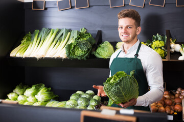 Positive man seller showing cabbage in grocery shop