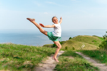 A little girl child cheerfully jumps into the air on a path in the middle of green meadows