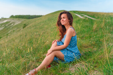 Beautiful young woman in a dress resting on the grass in a green meadow, amazing summer landscape