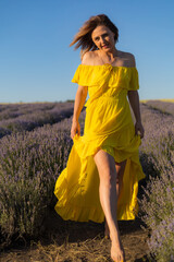 Beautiful and pretty young woman in yellow dress relaxes and enjoys walk in the lavender field at...