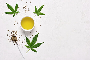 Hemp oil in bowl, leaves and seeds on white background, flat lay with copy space