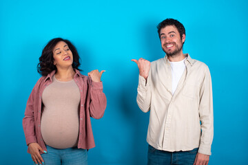 Charming young couple expecting a baby standing against blue background looking at copy space having advertisements