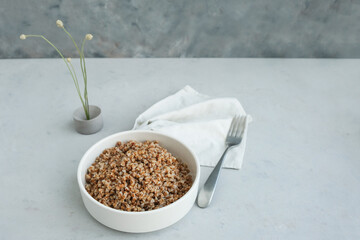 Bowl of buckwheat on a grey concrete background in minimalistic style. Concept of healthy food.