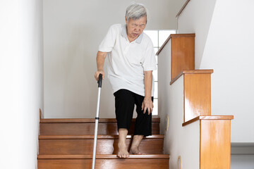 Senior woman holding her pain knee with hand while walking down the stairs,elderly suffering from...