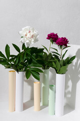 Vertical image of bright paper tubes and red, white peonies against bright wall