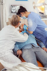 Obraz premium Senior woman dentist checking with mirror sick patient health. Medical nurse preparing for cleaning teeth, treating affected mass while sick man sitting on stomatology chair during examination
