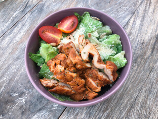 Fototapeta premium Green vegan salad from green leaves mix, vegetables, slices of chicken katsu. Top view on gray wood table.