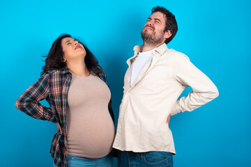 Obraz premium young couple expecting a baby standing against blue background got back pain