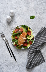 Lettuce leaves with avocado and chicken breast in a plate on a concrete background. View from above.