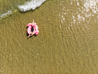 Woman on flamingo pool float in sea, drone aerial view. Summer holidays