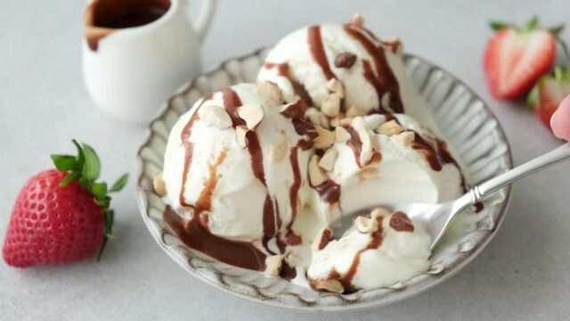 Eating vanilla ice cream with a spoon. Taking bite of ice cream sundae served with chocolate sauce and chopped nuts. Summer dessert
