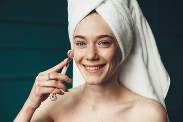 Woman with freckles smiling at camera while massaging her face with a derma roller