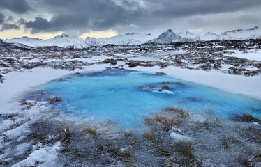 Winter landscape in north Norway: frozen swamp and snow covered mountains under dark sky