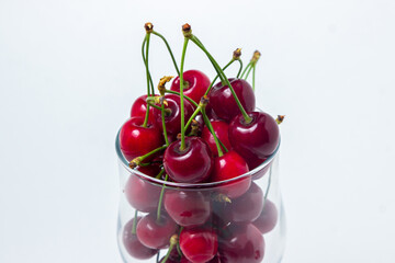 Red cherries in a glass on a white background. Sweet cherry with tails. Healthy food