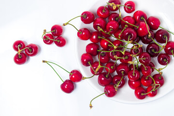 Obraz na płótnie Canvas Red cherries on a white plate on a white background. Sweet cherry with tails. Healthy food