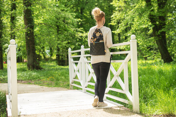 Young woman on a hike is walking in the park. He looks at the green trees from the white bridge. He has a backpack on. Active vacations. A trip in the forest or park. Natural conditions. 