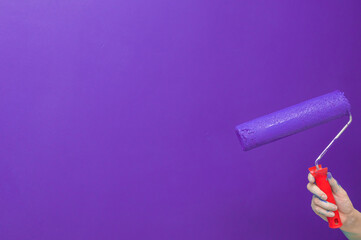 Hand with paint roller on light blue painted surface