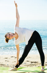 Athletic woman in white T-shirt is practicing set of stretching exercises on nature.