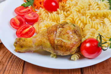 Roasted chicken leg against cooked spiral pasta, tomatoes, close-up