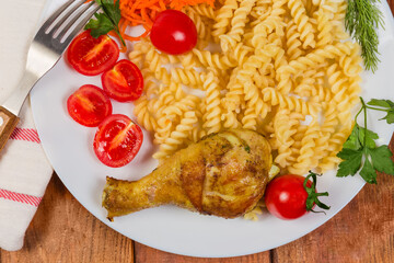 Roasted chicken leg with cooked spiral pasta, tomatoes, top view