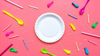 Ein runder weißer Pappteller, bunte Kerzen, Luftballones und Zuckerstreusel auf einem pinken...