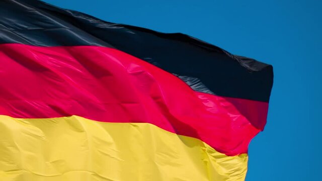 Close up large German flag waves in the wind on a blue sunny day filling frame