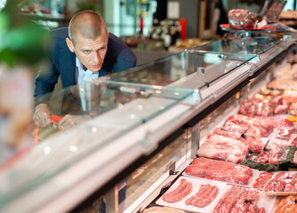 Man chooses and buys raw meat in a grocery supermarket