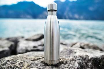 Close-up of steel eco thermo water bottle on the background of the lake in the mountains. Copy...